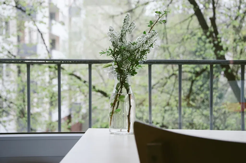 Coin repas installé sur un petit balcon, plante posée sur la table, garde-corps vitré