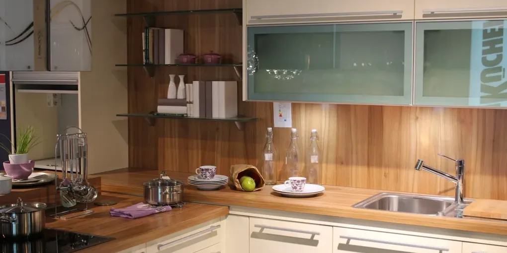 Petite cuisine en L avec plan de travail en bois, évier et meubles hauts vitrés