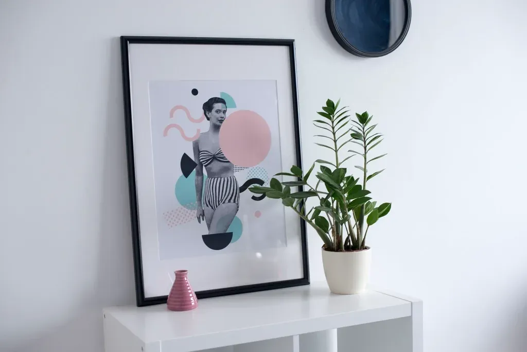 Cadre noir posé sur une console blanche à côté d’une plante verte et d’un petit vase